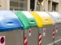 Fila de contenedores de reciclaje de Ecoembes en la calle: azul, verde, amarillo y grises.