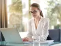 Kobieta w okularach pracuje na laptopie, szukając informacji, jak założyć działalność nierejestrowaną.