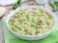 Un cremoso piatto di risi e bisi, con piselli freschi e cubetti di pancetta, servito in una ciotola bianca su un tovagliolo verde.