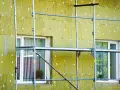 Installazione di un cappotto termico su un edificio, con ponteggi metallici che circondano la facciata isolata. La durata del cappotto termico è garantita da materiali di qualità.