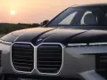 Przód luksusowego BMW M7 z podświetlaną atrapą chłodnicy i nowoczesnymi światłami, na tle zachodzącego słońca.