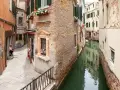 Un vicolo stretto e un canale a Venezia, con una donna e un cane seduti, tra i tanti **Venezia posti da visitare**.