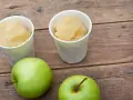 Zwei Becher mit erfrischendem Apfel Sorbet stehen neben zwei grünen Äpfeln auf einer Holzoberfläche.