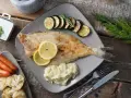 Gebratene Scholle, ein köstlicher Plattfisch, serviert mit Zucchini, Kartoffelpüree, Karotten und Blumenkohl. Zitronenscheiben und Kräuter garnieren das Gericht.