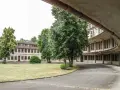 Alte Gebäude im olympisches Dorf Berlin, umgeben von Bäumen und Grünflächen. Eine Straße führt an einem geschwungenen Gebäude mit vielen Fenstern vorbei.