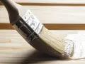 Pędzel rozprowadza lakier bezbarwny po drewnianej powierzchni, chroniąc ją i nadając jej połysk.
