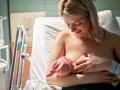 Uśmiechnięta mama karmi piersią noworodka. Pierwsze krople siary z piersi to cenny początek dla maluszka.