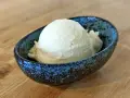 Ein Löffel cremiges Mandel Eis in einer blauen Schale auf Holztisch.