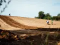 Des ouvriers travaillent sur un terrain en pente, utilisant des outils pour aplanir le sol. L'un mesure avec un mètre, l'autre pelle.