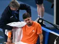 Tenisista z pomarańczową opaską na przedramieniu podczas Australian Open 2024 otrzymuje pomoc od fizjoterapeuty.