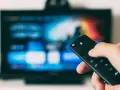 Dłoń trzymająca pilot do telewizora LG, ekran pokazuje menu. Dowiedz się, jak wyłączyć lektora w telewizorze LG.