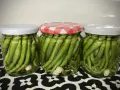 Tres frascos de vidrio llenos de piparras en vinagre, con ajos en el fondo. Uno tiene tapa a cuadros rojos y blancos.