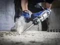 Wiertarka udarowa kruszy beton, generując pył. To narzędzie do ciężkich prac budowlanych.