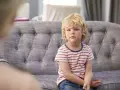 Chłopiec z blond włosami siedzi na kanapie w paski.
