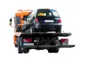 Pomarańczowy holownik zabiera uszkodzonego czarnego Renault Twingo po wypadku na autostradzie.