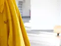 Gelbe Regenjacke hängt an einer Wand, bereit für die Regenjacke reparieren. Flecken auf dem Stoff deuten auf vergangene Abenteuer hin.