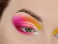 Oko z intensywnym makijażem w stylu cut crease, łączącym odcienie różu, pomarańczy i żółci.