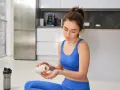 Femme en tenue de sport bleue prend des gélules, espérant un vitamine b12 effet immédiat pour son bien-être.