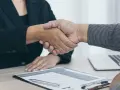 Dos personas se dan la mano sobre un escritorio con un currículum y un portátil. Es el final de una entrevista en francés.