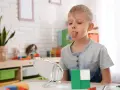 Chłopiec ćwiczy język przed lustrem, pracując nad **dyslalią**. W tle zabawki i rośliny.