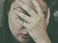 Kobieta zakrywająca twarz dłońmi, z widocznymi ustami i fragmentem oka.