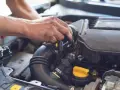 Ręce mechanika pracują przy silniku. Widoczny jest czarny przewód dolotowy i żółta zakrętka. p0101.