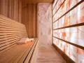 A serene salt sauna with a wooden bench, towels, candles, and a wall of glowing Himalayan salt bricks.