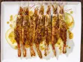 Gamberoni al forno dorati e croccanti, serviti su fette di limone e conditi con un sugo saporito.