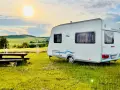 Przyczepa Caravelair zaparkowana na łące o zachodzie słońca. W tle malownicze wzgórza i pola.