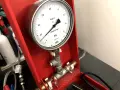 Manometr do prób szczelności gazu, z tarczą wskazującą ciśnienie w MPa. Urządzenie jest częścią czerwonej skrzynki narzędziowej.