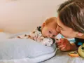 Mama pochyla się nad dzieckiem, które leży na poduszce. Szybki oddech u noworodka może być naturalny, ale czujność rodzica jest ważna.