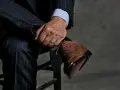 Un uomo con un abito gessato blu scuro e una camicia azzurra indossa eleganti scarpe stringate marroni.