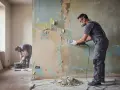 Operai in azione per la rasatura del muro, rimuovendo la vecchia pittura scrostata con attrezzi specifici.