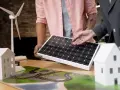 Model domu, wiatraka i panelu słonecznego na stole. Dwie osoby omawiają projekt, być może przyszłego prosumenta wirtualnego.
