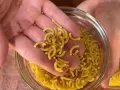 Mano sosteniendo fideos cortos y curvos sobre un bol de fideos similares.