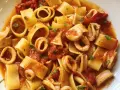 Pasta con calamares, un plato italiano lleno de sabor. Los calamares se mezclan con trozos de tomate y perejil fresco, creando una deliciosa combinación.