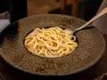 Pyszne cacio e pepe na czarnym talerzu, z widocznym młynkiem do pieprzu i solniczką w tle.