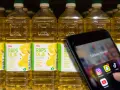 En hand håller upp en mobil med sociala medier-appar. Bakom syns rader av rapsoljeflaskor, där en del anser att rapsolja är farligt.