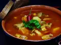 Pyszna zupa gulaszowa Ewy Wachowicz z kawałkami mięsa, ziemniaków i papryki, udekorowana papryczką chili i natką pietruszki. Podana z chlebem.