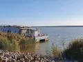 Ein Katamaran namens "Barbara" liegt am Ufer des Schlabendorfer Sees, umgeben von Schilf und Steinen.