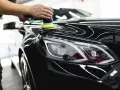 A person uses a polisher to wax a shiny black car, bringing out its deep gloss.