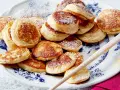 Ein Teller voller goldbrauner Poffertjes, bestäubt mit Puderzucker. Dieses Poffertjes Rezept ist ein Genuss!