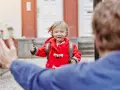 Kleines Mädchen im roten Mantel mit Rucksack rennt auf jemanden zu. Ein schönes Beispiel für das Wechselmodell bei Kindern.