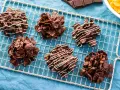 Sei dolcetti croccanti al cioccolato, simili a rose del deserto, raffreddano su una griglia. Alcuni sono decorati con sottili fili di cioccolato bianco.