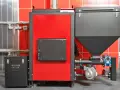 Nowoczesny piec na pellet, idealny jako jaki piec na pellet do domu 120m2. Czerwono-czarna obudowa, zasobnik na pellet i elementy instalacji.