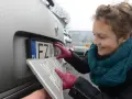 Kobieta w czerwonych rękawiczkach montuje tablicę rejestracyjną.