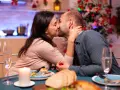 Romantyczny wieczór, kolacja przy świecach i choince. Para celebruje dzień pocałunku, mężczyzna trzyma w dłoni czerwone pudełeczko.