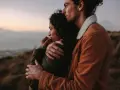 A couple embraces, looking out at a hazy landscape. This image shows how to feel more connected through shared moments and physical closeness.