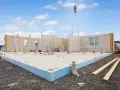 Budowa domu z prefabrykatów. Widać fundament z keramzytobetonu, ściany zewnętrzne i pracującą na budowie żuraw.