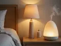 Mesita de noche con lámpara, difusor emitiendo vapor y un pequeño frasco. La humedad del 70% en la habitación crea un ambiente acogedor.